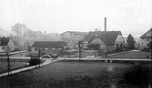 Möbelfabrik Pecher in den 1960er-Jahren, parallel zur quer durch das Bild verlaufenden Herforder Straße ist der Lagerschuppen für das Holz zu sehen. Nach links unten verläft der Zugang zur Siedlung Auf dem Pulsfeld